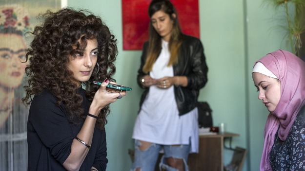 De drie hoofdrolspeelsters in Bar Bahar. Een spreekt haar mobiele telefoon in terwijl ze die horizontaal vlakbij haar mond houdt.
