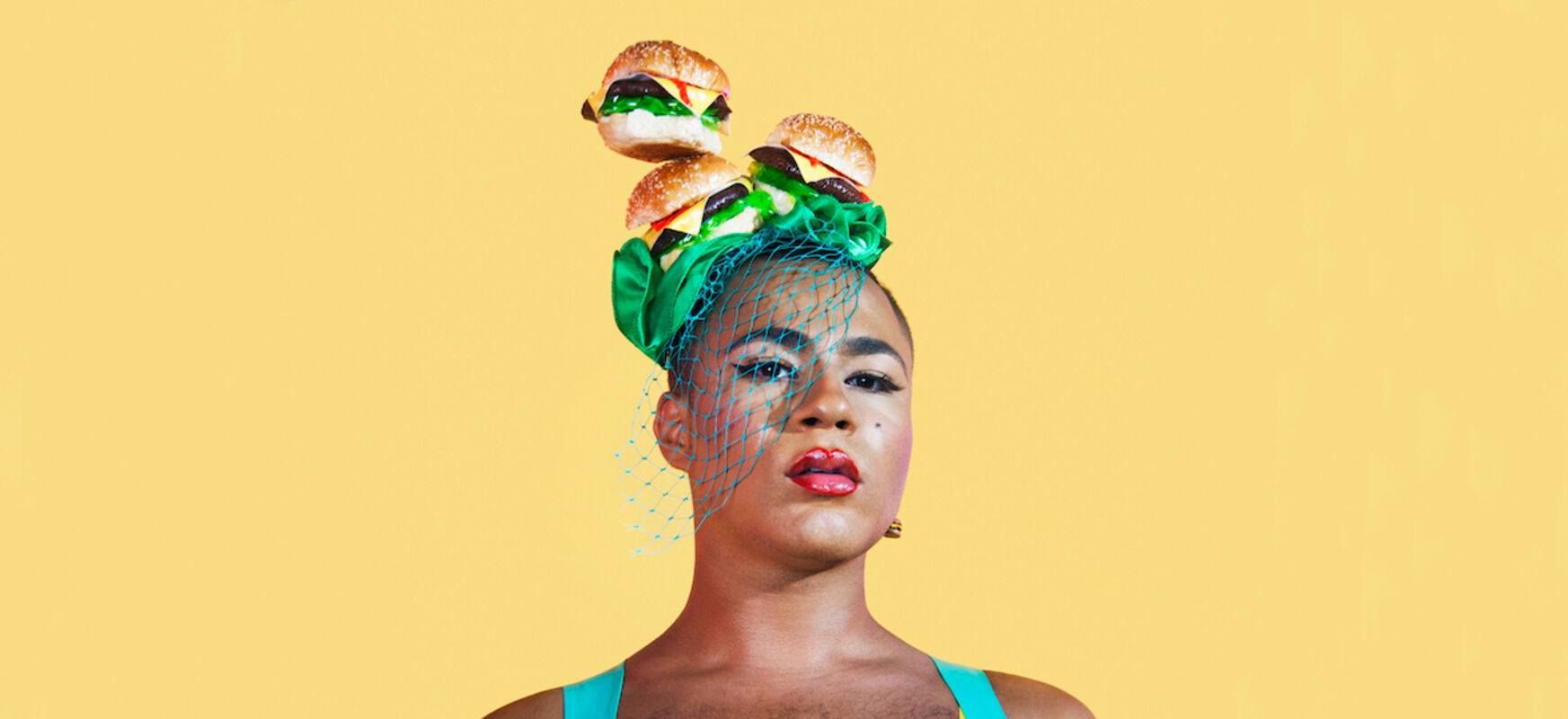 Portrait of the head of the performance artist and activist Travis Alabanza. They is wearing a hat decorated with burgers.